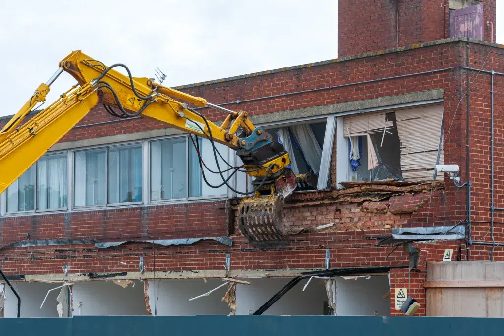 Excavator cu grifă demolează fațada de cărămidă a unei clădiri