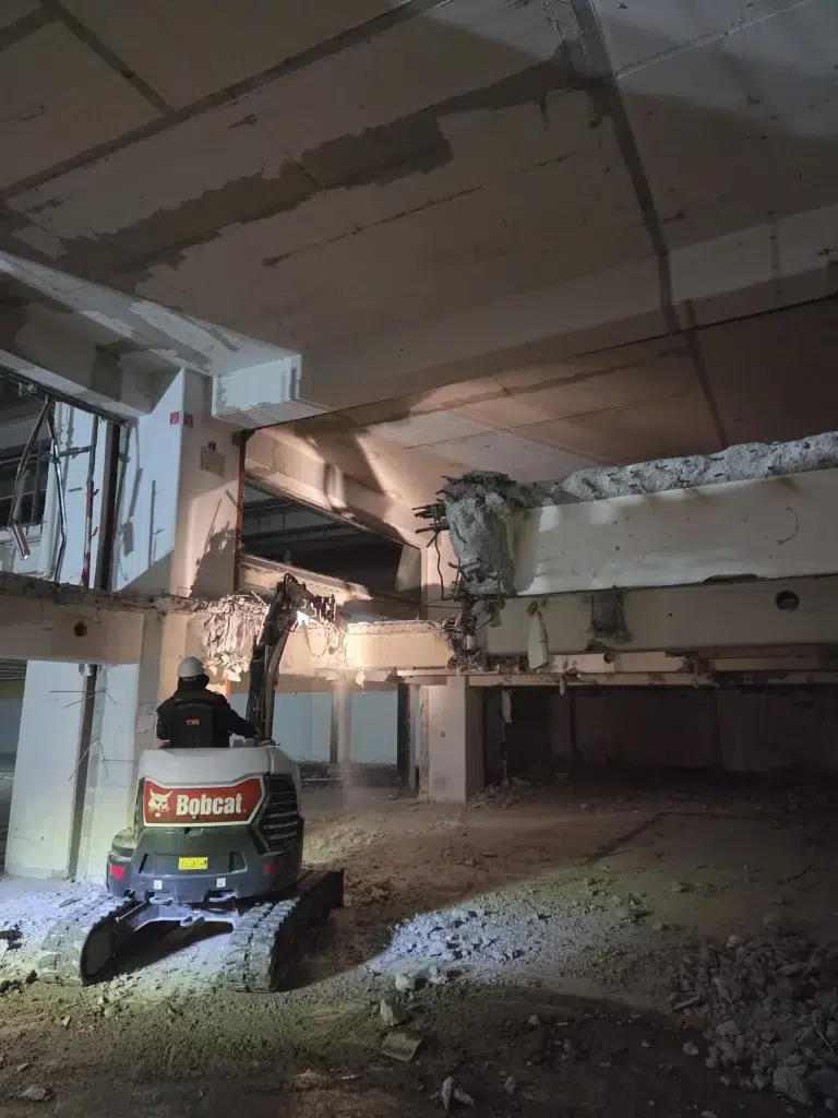 Miniexcavator Bobcat demolează grinzi de beton în interiorul unei clădiri dezafectate